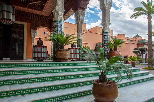 02-11-2015 Garden of 5 star hotel  and casino La Mamounia  with potted plants and  stairs to casino or hotel - \ninteresting buildng  with moroccan tiles  in Marrakech. Background - building of hotel of brown color