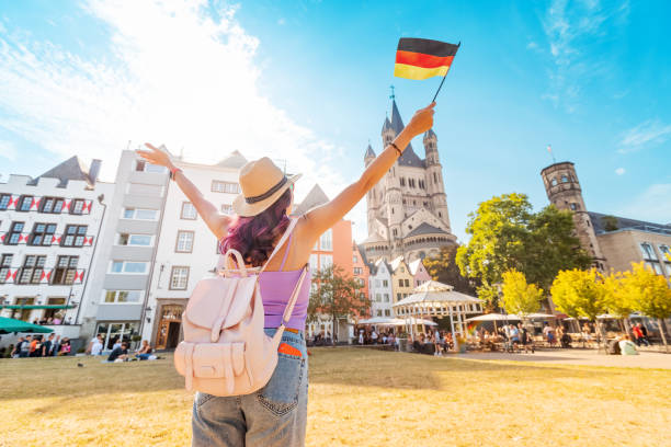 A young happy tourist or student girl with a German flag at the old town or Altstadt in Cologne fish market square. Studying language abroad and traveling concept stock photo