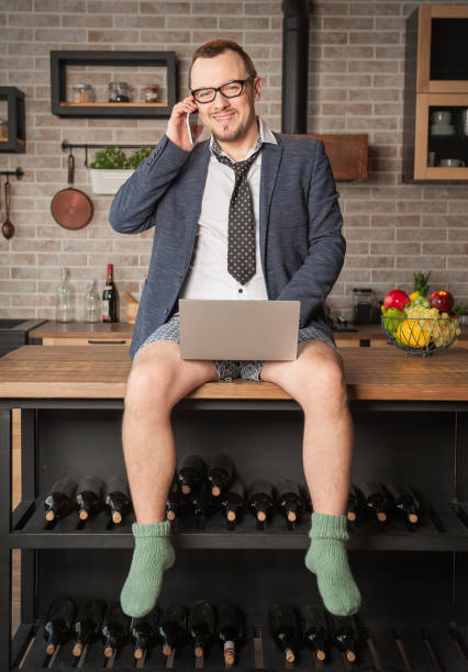 Happy man wearing suit and underpants working at home online siting on the kitchen table stock photo