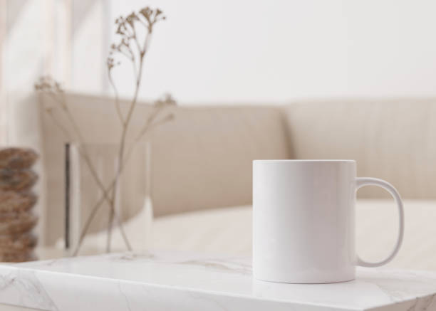 istock White mug mock up. Blank template for your design, advertising, logo. Close-up view. Copy space. Cup standing on coffee table in modern interior. Minimalist coffee cup mockup. 3D rendering. 1450106452