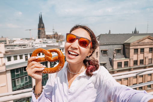 Happy girl tourist with a pretzel on the background of an Cologne cathedral building. Travel and tourism in Germany and Rhineland