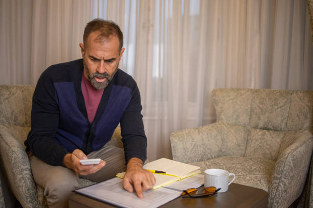 istock Mid adult man using calculator while going through bills and home finances 1450112307
