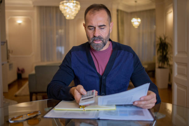 istock Mid adult man using calculator while going through bills and home finances 1450112872