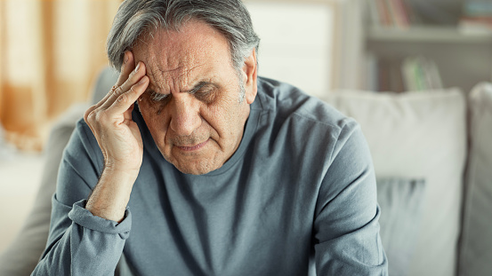 Old man holding his forehead sitting alone at home