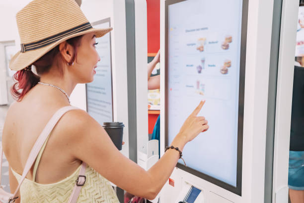 여성 고객이 터치스크린 단말기 또는 셀프 서비스 키오스크를 사용하여 패스트푸드점에서 주문합니다. 자동 기계 및 전자 결제 - 터치스크린 뉴스 사��진 이미지