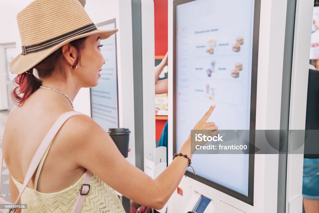 A female customer uses a touchscreen terminal or self-service kiosk to order at a fast food restaurant. Automated machine and electronic payment Kiosk Stock Photo