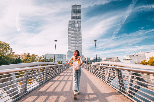 Tourist girl walking by footbridge in MediaPark in Cologne city - it is a popular and modern district with pond, futuristic skyscrapper with media companies