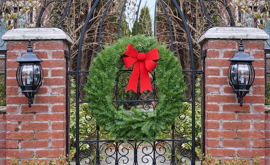 Garden gate with brick pillars decorated with Christmas wreath made of pine branches and red bow