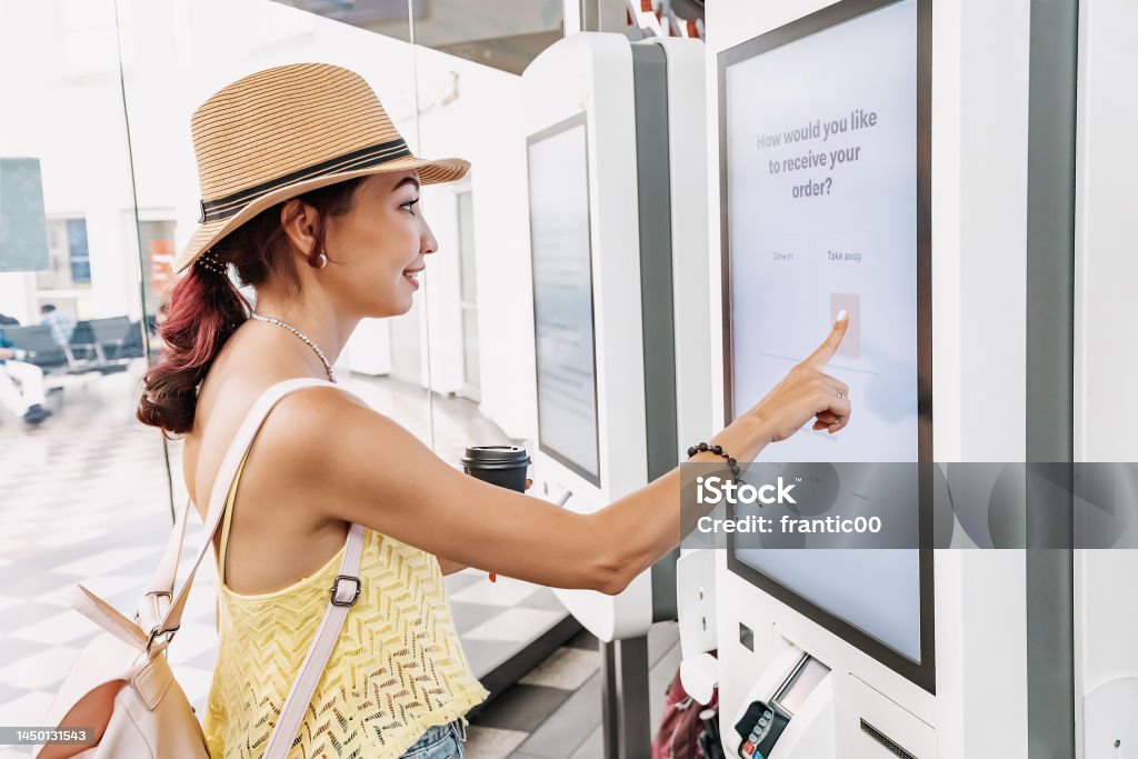 A female customer uses a touchscreen terminal or self-service kiosk to order at a fast food restaurant. Automated machine and electronic payment Point Of Sale Stock Photo