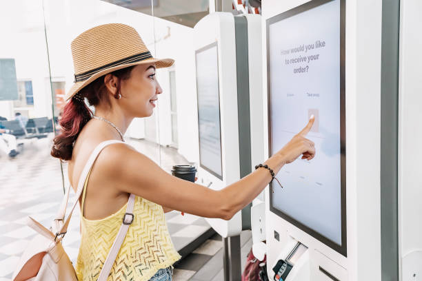 A female customer uses a touchscreen terminal or self-service kiosk to order at a fast food restaurant. Automated machine and electronic payment stock photo