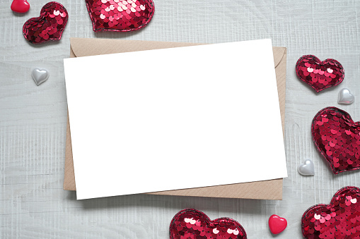 Blank white greeting card with brown envelop and hearts on marble table. Mockup valentines day concept