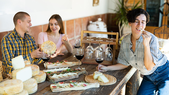 Young Hispanic woman enjoying delicious artisanal hard goat cheese with red wine at tasting in artisanal cheese factory