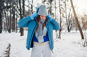 Portrait of young woman putting on blue coat walking in snowy winter park. Warm clothes for cold weather