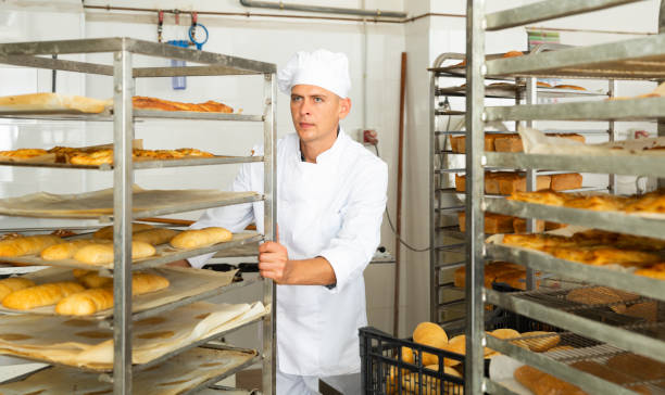 istock Male baker carrying rack trolley with bread 1450137460