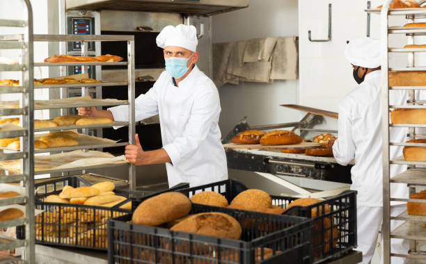 istock Man in protective mask transporting cart with bread in bakery 1450137461