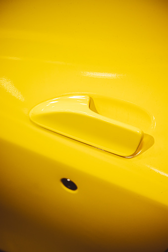 Close up shot of a modern door handle of a yellow car.