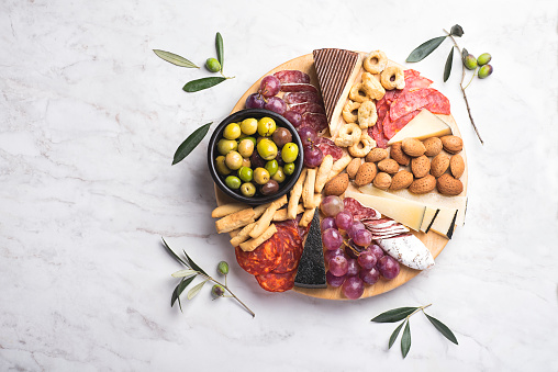 Appetizers boards with assorted  delicatessen cheese, salami, grape and nuts. Charcuterie and cheese platter, Spanish style and ingredients: olives, Pimientos, Chorizo, picos, cheese Semicurado. Top view, white table. copy space