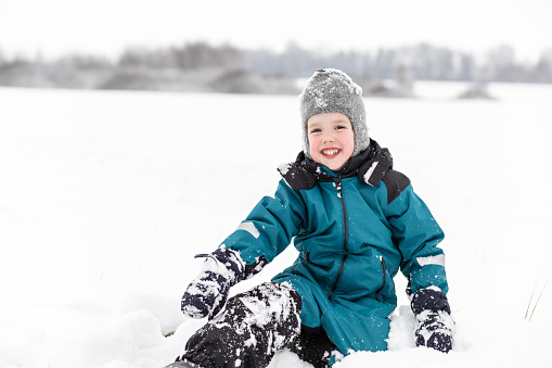 Cheerful 5 year old white boy playing in the snow on a winter walk