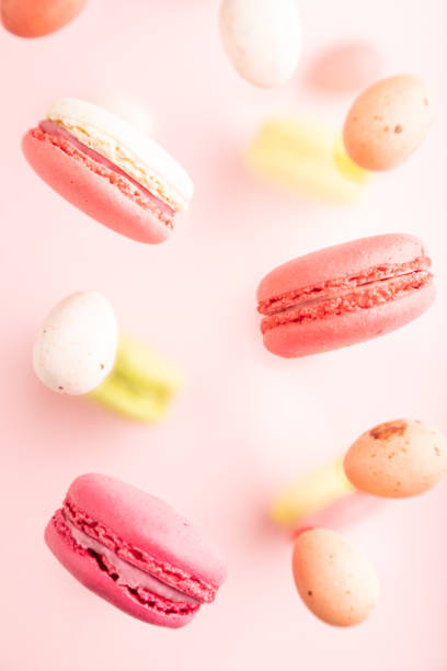 istock Different colors flying macaroons and chocolate eggs frozen in the air on blurred pink background. top view, close up. 1450158013