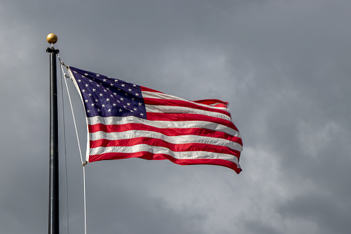 An American flag on a flag pole blowing in the wind on a cloudy day