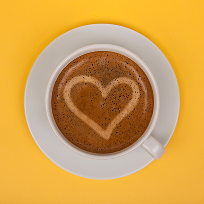 Coffee cup with heart shape on yellow background