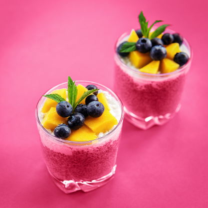 Two glasses of Chia pudding with coconut cream, mango and blueberry on viva magenta background, top view. Healthy food, raw, vegan. Toned image.