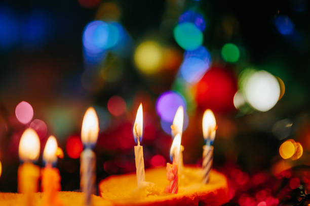 Close up fire of candles on a bright blurred background. Colored light from bulbs of garlands illuminates the holidays. Bokeh, selective focus.