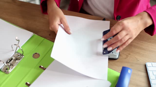Female hands of accountant or secretary are punching holes with hole punch in documents in office