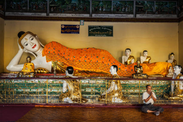 man meditating near statue of recumbent buddha in shwedagon paya pagoda - paya imagens e fotografias de stock