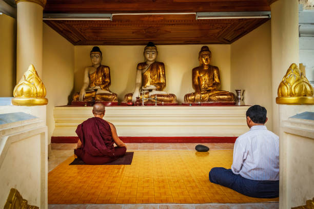 man and buddhist monk meditating and worshipping statues of buddha in shwedagon paya pagoda - paya imagens e fotografias de stock