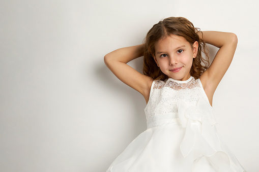 Portrait of a cute smiling girl wearing white dress, close-up. Happy child girl on white background with copy space