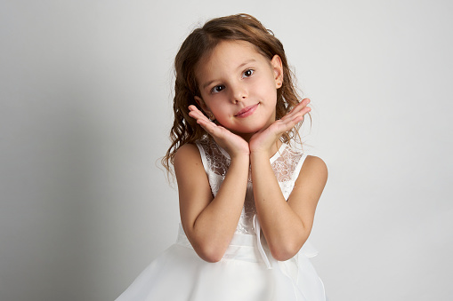 Portrait of a cute smiling girl wearing white dress, close-up. Happy child girl on white background with copy space