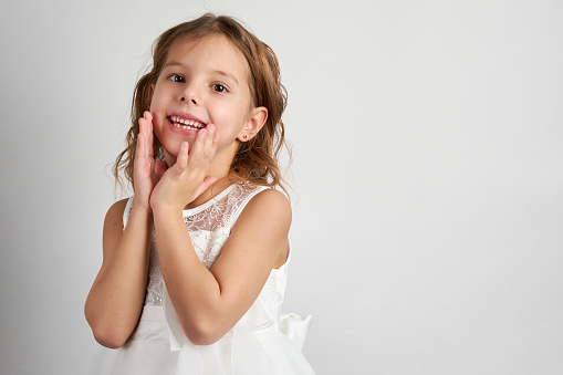 Portrait of a cute smiling girl wearing white dress, close-up. Happy child girl on white background with copy space