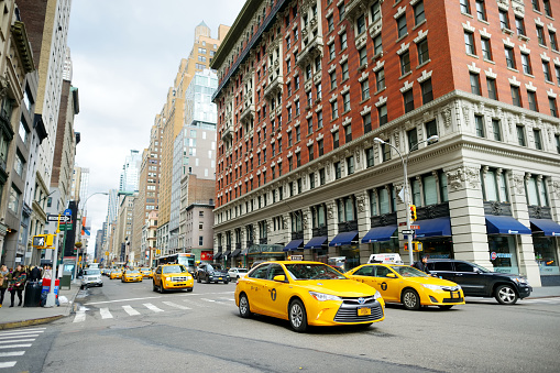 New York - March 16, 2015: Yellow taxi cabs and people rushing on busy streets of downtown Manhattan. Taxicabs with their distinctive yellow paint are a widely recognized icon of New York City.