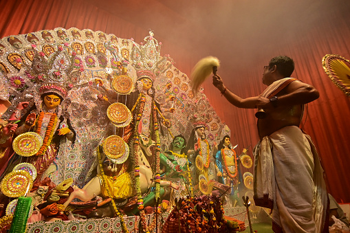 Howrah, India -October 13, 2021 : Hindu Priests worshipping Goddess Durga with ghanta, chamor and hand fan. Ashtami puja aarati - sacred Durga Puja ritual - shot at night.