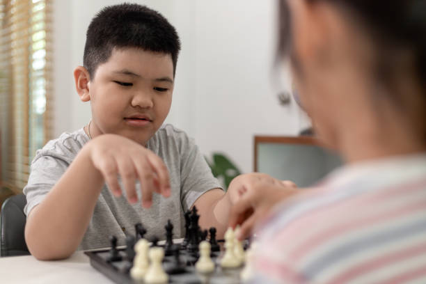 el niño y la niña están jugando al ajedrez en casa. niños jugando al ajedrez - chess skill concentration intelligence fotografías e imágenes de stock