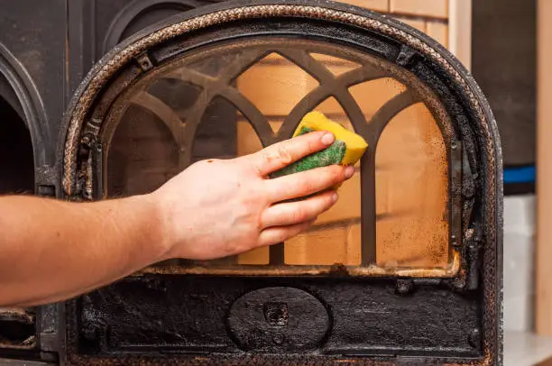 Maintenance of the stove door with glass after the heating season. Removing carbon deposits with a sponge