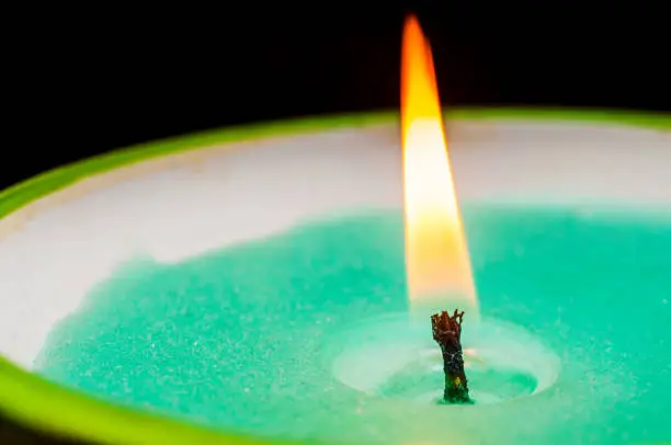 Photo of Burning candle wick with green wax close-up on black background. Macro shooting.