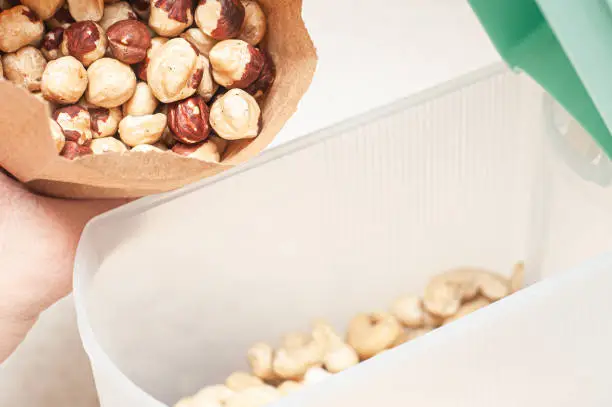 Pour hazelnuts in one bowl with cashew nuts to create an assortment of nuts for a balanced diet.