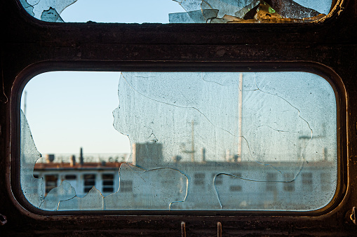 Cracked dirty window of an abandoned ship with a broken piece of glass. Focus in the foreground.