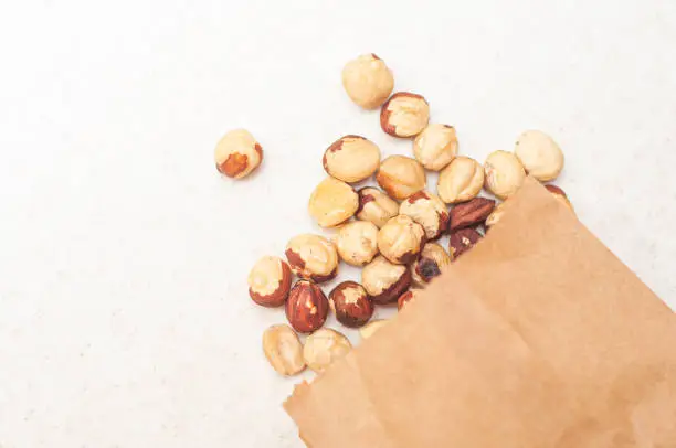 Poured beautifully laid out hazelnuts from a brown paper bag on a white table.