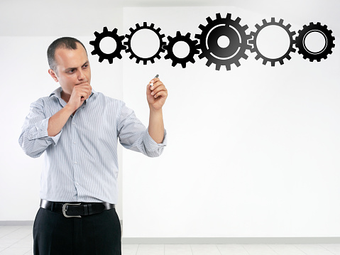 Businessman drawing cogwheels on a transparent wipe board