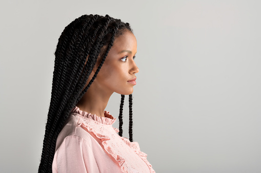 Side view of young African American female in vintage pink blouse with long braided hair looking away against gray background