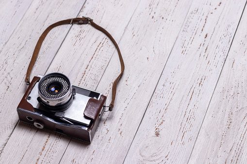 Old retro camera with a small leather strap. On a wooden background.