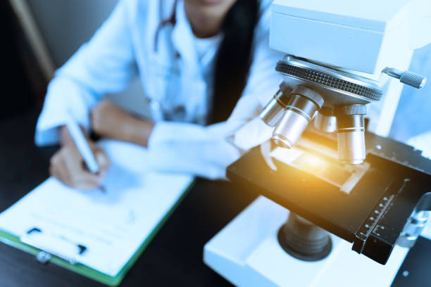 Female medical Doctor or research scientist looking through a microscope in a laboratory.science experiments,laboratory glassware containing chemical liquid for researching biology chemistry samples stock photo