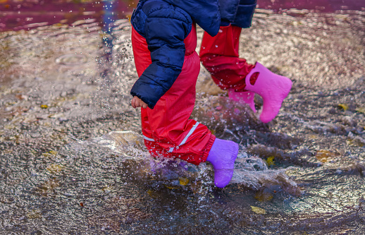 two children walking through a puddle of water with their boots on a rainy day
