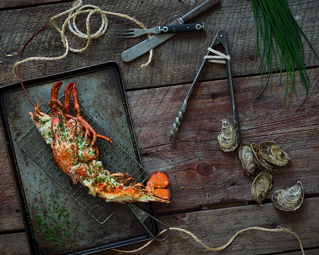 rustic lobster thermidor on a wooden surface with oysters and chives and kitchen utensils