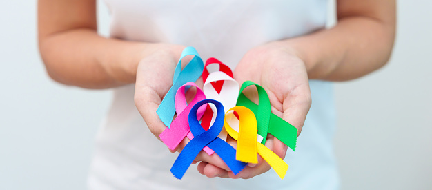 World cancer day, February 4. Hand holding blue, red, green, white, pink, navy blue and yellow ribbons for supporting people living and illness. Healthcare and Autism awareness day concept