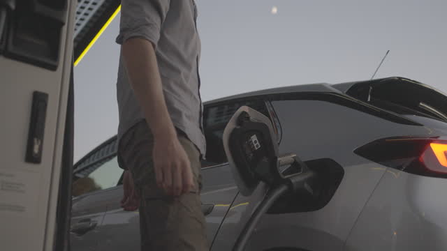 Detail of hand plugging in electric car at night