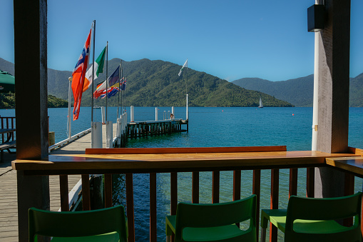 Pier with flags projecting into scenic bay surrounded by bush clad hills of Marlborough Sounds, New Zealand.